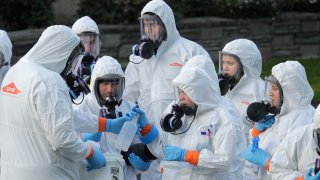 In this March 11, 2020, file photo, workers from a Servpro disaster recovery team wearing protective suits and respirators are given supplies as they line up before entering the Life Care Center in Kirkland, Washington, to begin cleaning and disinfecting the facility.