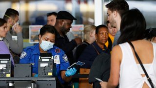 In this Saturday, March 14, 2020 file photo, a Transportation Security Administration agent hands a passport back to a traveler as she screens travelers, at a checkpoint inside an airline terminal at John F. Kennedy Airport in New York.