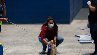 A deported woman looks at her family as she picks up the food they brought her, at the site where Guatemalans returned from the U.S. are being held in Guatemala City, Friday, April 17, 2020.