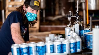 Colin Conroy operates a labeling machine as cans of "Fauci Spring" beer are labeled at Wild Heaven Beer on Thursday, April 30, 2020, in Avondale Estates, Ga.
