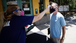 In this June 11, 2020, file photo, health services worker Summer Deibert, left, checks the temperature of James McCluskey, right, as he arrives for work before the reopening of the San Diego Zoo in San Diego.