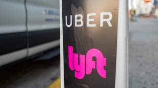 Close-up of vertical sign with logos for ridesharing companies Uber and Lyft, with wheels of a car in the background, indicating a location where rideshare pickups are available in downtown Los Angeles, California, October 24, 2018. (Photo by Smith Collection/Gado/Getty Images)