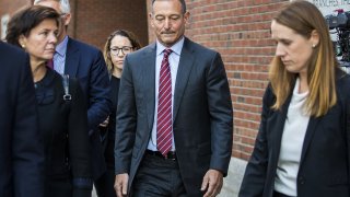 In this Monday, Oct. 21, 2019, photo, Douglas Hodge, former chief executive office of Pacific Investment Management Co., center, exits federal court in Boston on Monday, Oct. 21, 2019. Hodge, accused of using a middleman to cheat his kids’ way into elite colleges, pleaded guilty to fraud and money-laundering conspiracy charges, the first in a flurry of plea changes as the government’s prosecution of the U.S. college admissions scam gathers steam.