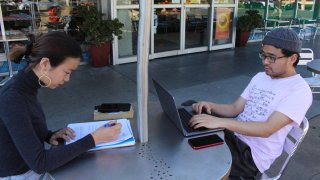 International students Yaqing "Victoria" Yang and Ende Shen of China study together at a sidewalk table in the Silicon Valley city of Palo Alto