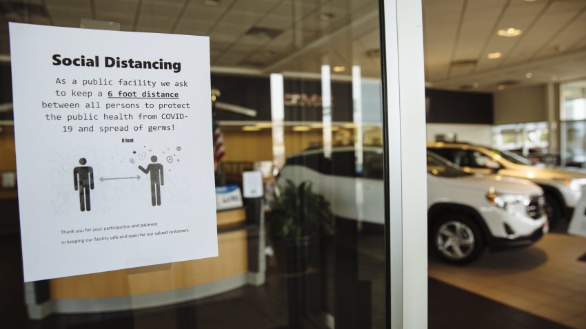 A sign advising customers to practice social distancing is displayed on the door of a General Motors Co. Buick and GMC car dealership