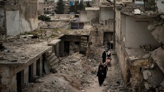 In this Thursday, March 12, 2020 photo, women walk in a neighborhood heavily damaged by airstrikes in Idlib, Syria.