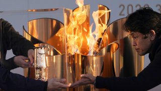 In this March 25, 2020, file, photo, officials light a lantern from the Olympic Flame at the end of a flame display ceremony in Iwaki, northern Japan.