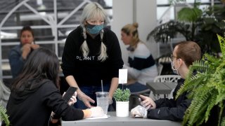 In this May 18, 2020, file photo, server Katie Maloney, of Providence, Rhode Island, center, wears a mask out of concern for the coronavirus while serving people in an outdoor seating area at Plant City restaurant in Providence, Rhode Island.