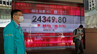 In this April 15, 2020, file photo, men wearing face masks stand in front of an electronic board showing Hong Kong share index outside a local bank in Hong Kong.