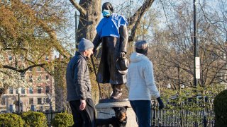 This April 17, 2020, file photo shows a mask and medical shirt draped over the statue of historian and minister Edward Everett Hale in an empty Boston Public Garden.