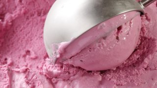 A metal ice cream scooper scooping up one spoonful of pink ice cream.