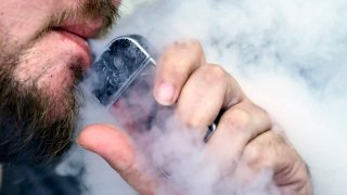 Close-up image of a man with a beard using a vaping device