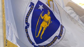 BOSTON, MA – JUNE 7: The state flag of Massachusetts, depicting a Native American under an arm wielding a sword, hangs in front of the Massachusetts State House in Boston on June 7, 2019. There has been an ongoing effort to change the flag, under fire for decades, but now Cambridge city officials are taking a stand. City councilors voted last month to support a bill in the State House that proposes creating a commission to redesign the flag, which Native Americans and others say is offensive. (Photo by John Tlumacki/The Boston Globe via Getty Images)