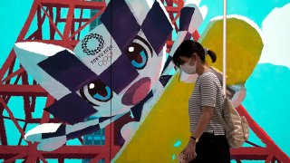 A pedestrian wearing a protective mask walks past an advertisement for the now-postponed Tokyo 2020 Olympic and Paralympic Games in Tokyo, Japan, June 8, 2020.