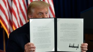 In this Aug. 8, 2020 file photo, President Donald Trump signs an executive order during a news conference at the Trump National Golf Club in Bedminster, N.J.