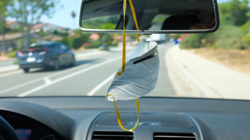 A facemask hangs from the rearview mirror of a car.