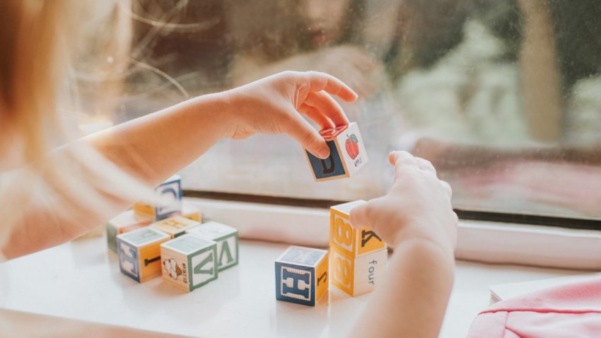 A child plays with blocks in front of a window.