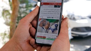 A man holds a phone while reading a story published on Tasnim News Agency's website about the recent news of a US-brokered deal between Israel and the UAE to normalise relations, in Iran's capital Tehran on August 14, 2020.