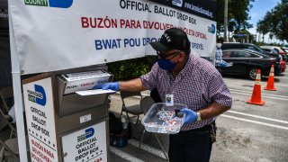 In this Aug. 18, 2020, file photo, poll workers help a voter put their mail-in ballot in an official Miami-Dade County drive- thru ballot drop box during Florida Primary Election amid the coronavirus pandemic, in Miami, Florida.
