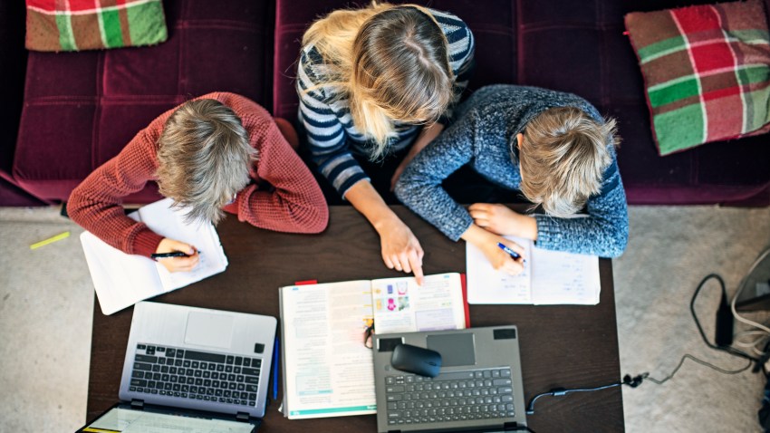 Mother helping sons with homeschooling at home during COVID-19 pandemic.