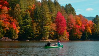 Two people and a dog canoe in Waterbury, Vermont, as the trees change colors in the fall