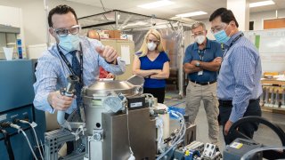 Astronaut Kate Rubins, center, and support personnel review the Universal Waste Management System, a low-gravity space toilet, in Houston