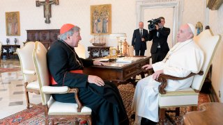 Pope Francis, right, sits at a table with Cardinal George Pell