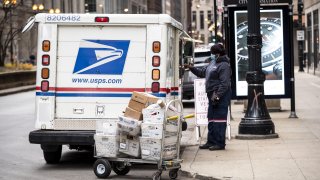 A United Postal Service (USPS) worker unloads packages in Chicago, Illinois, U.S., on Monday, Nov. 30, 2020. Online shoppers in the U.S. are expected to drop a record-busting $12.7 billion on Cyber Monday -- the busiest e-commerce day of the year -- presenting a valuable opportunity for retailers whose websites, customer service departments and delivery operations can withstand the period of crushing traffic.