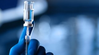 A medical hand in a glove holds an ampoule with a vaccine and a syringe with illustration