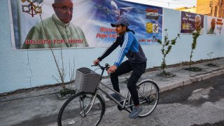 In this Feb. 27, 2021, file photo, a boy cycles past a poster welcoming Pope Francis, who is expected visit Iraq in March, hanging on the wall of the Chaldean Catholic Church of St. Joseph in the capital Baghdad.