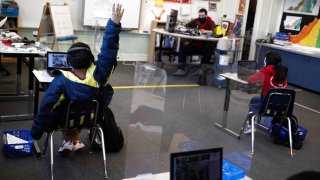 Chrystopher Camey Lopez raises his hand to ask a question from a socially-distanced desk during an in-person hybrid learning day at the Mount Vernon Community School in Alexandria, Virginia,
