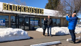 FILE - In this March 11, 2019, file photo Debby Saltzman, of Bend, Ore., poses for a photo, in front of the last Blockbuster store with her twin brother, Michael, visiting from Melbourne, Australia, in Bend, Ore. Taking the photo is Saltzman's husband, Jeremy Saltzman. The new Netflix movie called The Last Blockbuster that began airing March 15, 2021 is generating interest in the store, which became the last Blockbuster location on Earth when a location in Perth, Australia shut its doors in 2019.