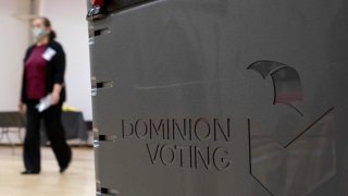 A worker passes a Dominion Voting ballot scanner while setting up a polling location at an elementary school in Gwinnett County, Ga., outside of Atlanta on Monday, Jan. 4, 2021, in advance of the Senate runoff election.