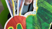 This file photo shows Eric Carle stand with a large cutout of the iconic image from his children's book, "The Very Hungry Caterpillar," at his museum in Amherst, Mass.