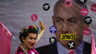 An Israeli protester waves towards a poster depicting Prime Minister Benjamin Netanyahu during a demonstration against him in front of his residence in Jerusalem, on June 12, 2021, a day ahead of a vote on a new government at the Knesset which would end his rule.