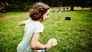 Girl runs with a water balloon on a green lawn