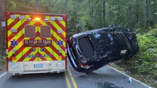 A car with a shattered back windshield wedged between a hill and an ambulance