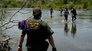 FILE - In this June 15, 2021, file photo a Border Patrol agent watches as a group of migrants walk across the Rio Grande on their way to turn themselves in upon crossing the U.S.-Mexico border in Del Rio, Texas. The Biden administration proposed Wednesday, Aug. 18, to change the way asylum claims are handled, aiming to cut a huge backlog of cases from the Southwest border that has resulted in people waiting years to find out if they will be allowed to stay in the U.S.