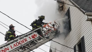 firefighters on ladder truck spray water into window of smoking home in Lynn