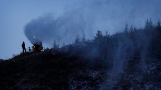 A person works at a snow making machine on a hill overlooking cross-country skiing practice before the 2022 Winter Olympics, Feb. 2, 2022, in Zhangjiakou, China.