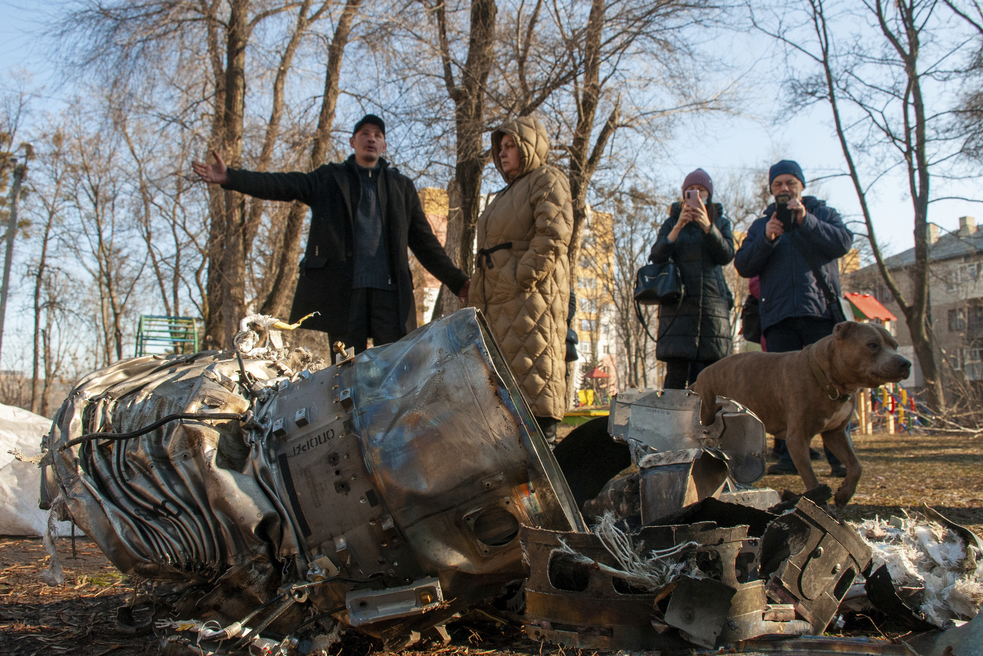 People stand next to fragments of military equipment on the street in the aftermath of an apparent Russian strike in Kharkiv, Ukraine, Thursday, Feb. 24, 2022.