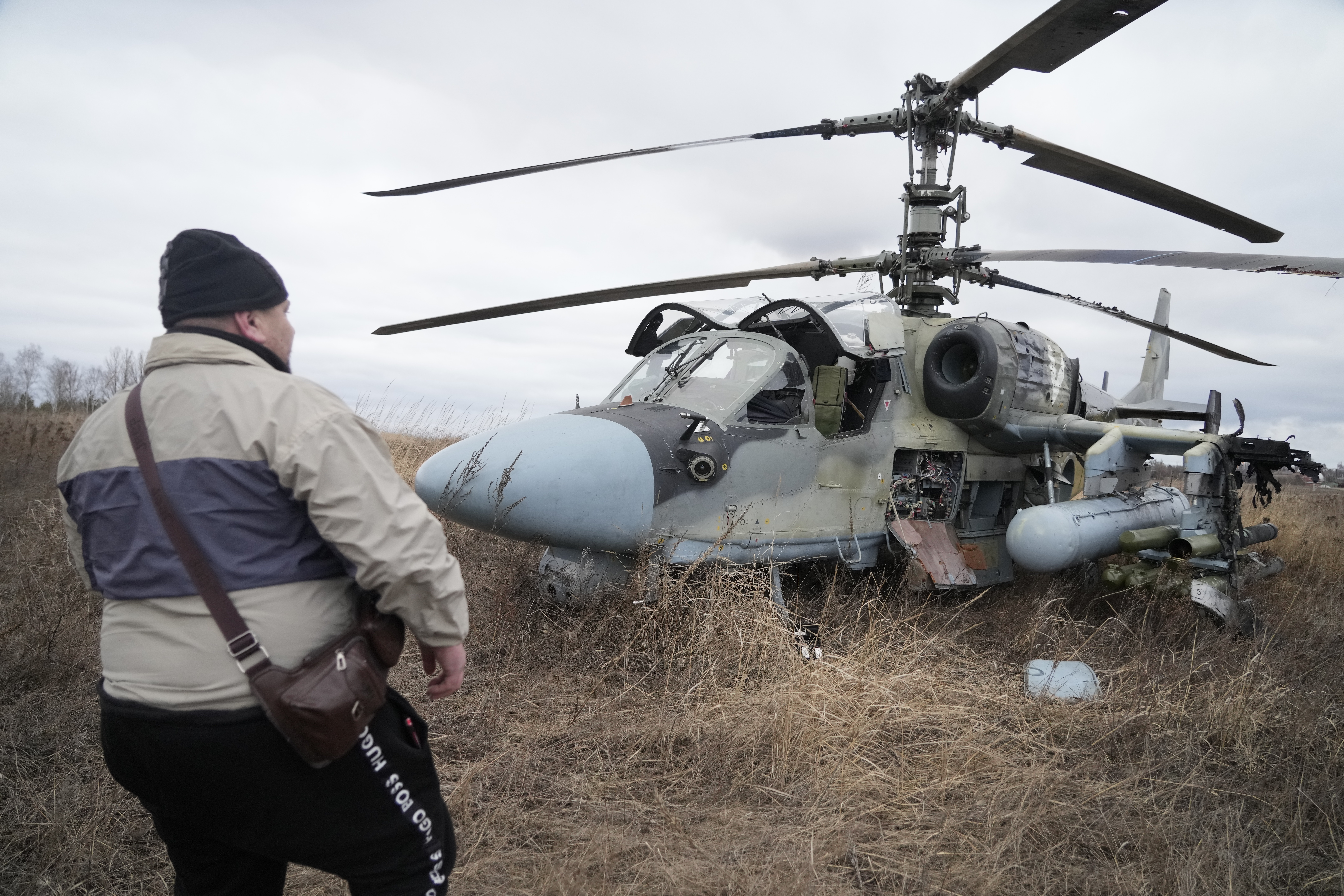 A man stands in front of a Russian Ka-52 helicopter gunship that is seen in a field after a forced landing outside Kyiv, Ukraine, Thursday, Feb. 24, 2022.