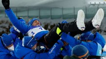 Team members toss gold medallist Quentin Fillon Maillet of Team France as they celebrate on the podium