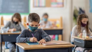 boy sitting at desk wearing a mask at school