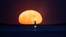 The strawberry supermoon rises over the Boston Light in Boston Harbor on Tuesday, June 14, 2022.