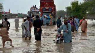 FILE - People navigate through a flooded road caused by heavy monsoon rains