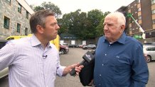 A reporter holds a microphone out to a man while the pair stand in a parking lot