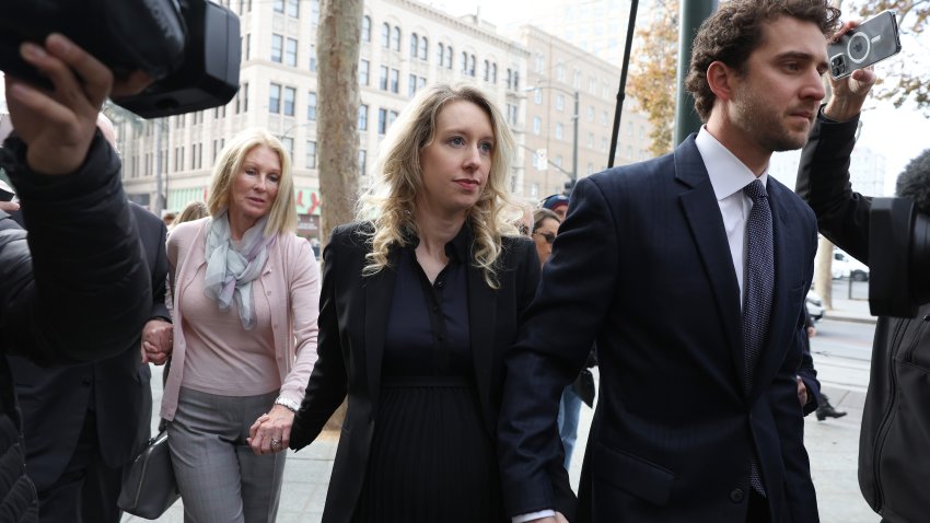 Former Theranos CEO Elizabeth Holmes (C) arrives at federal court with her partner Billy Evans (R) and mother Noel Holmes on November 18, 2022 in San Jose, California. Holmes appeared in federal court for sentencing after being convicted of four counts of fraud for allegedly engaging in a multimillion-dollar scheme to defraud investors in her company Theranos, which offered blood testing lab services.