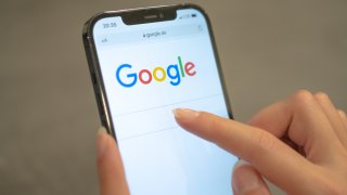 A woman holds her cell phone, which shows the Google page in the browser.