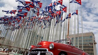 FILE - A classic American convertible car passes beside the United States embassy as Cuban flags fly at the Anti-Imperialist Tribune